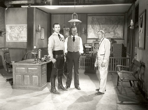 Pat Conway as Sheriff Clay Hollister and Richard Eastham as TOMBSTONE EPITAPH editor Harris Claybourne on the set of the sheriff’s office for ABC’s “Tombstone Territory”. The other man could be a director or even the set decorator.