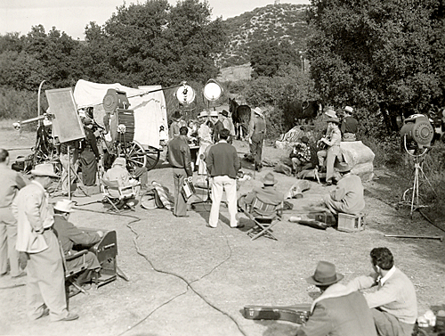 On location for a Jimmy Wakely Western. Lee Lasses White and Jimmy Wakely can be seen wearing the white hats in front of the lights and boom mike. 