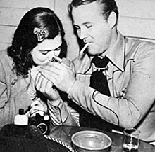 Wayne Morris lights a cigarette for...isn’t that Sigrid Gurie? 