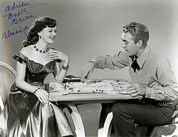 Adrian Booth and Forrest Tucker engage in a game of Monopoly between scenes on a Western film. 