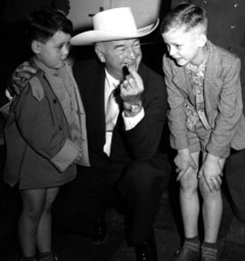 William Boyd, Hopalong Cassidy, presents Hoppy coins to a couple of young fans as he and his wife Grace arrived at the Rhein-Main Airport in Frankfurt, Germany, on August 27, 1954, during the European segment of their around-the-world vacation. (Thanx to Joel O'Brien.)