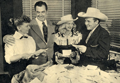 Johnny Mack Brown, Reno Browne and Whip Wilson stand with Rae Lynn as they judge the winners of the MOVIE THRILLS magazine Whip Wilson “Name the Horse” contest in November 1950. The name Rocket was the winner.